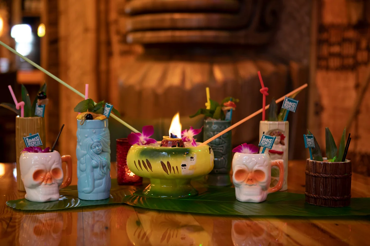 Colorful tiki cocktails in skull and tiki mugs lined up on the Bamboo Room bar
